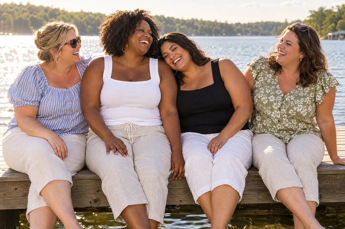 Four curvy friends laughing on a lake dock in summer, two in the White and Black bra tanks