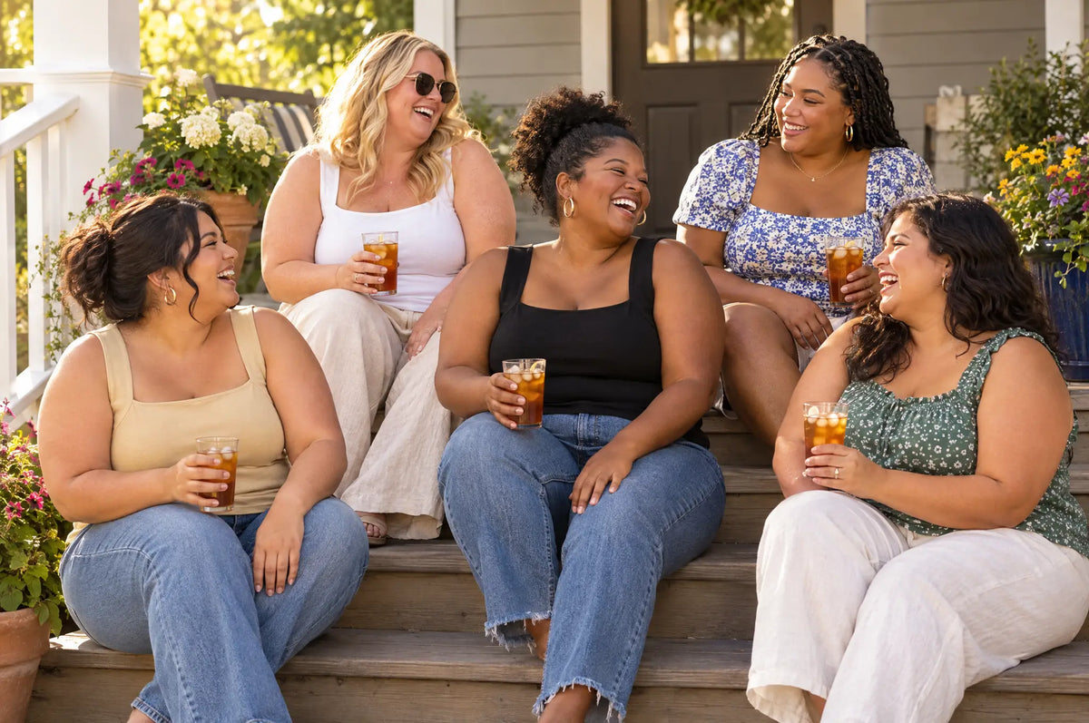 Five curvy friends with iced tea on porch steps, three in the Beige, White and Black bra tanks