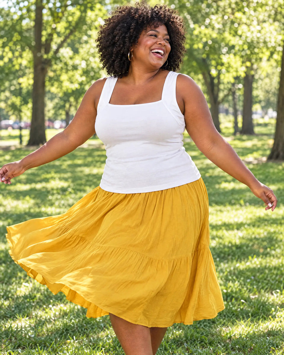 Curvy woman twirling in a sunny park in the White bra tank and a yellow skirt