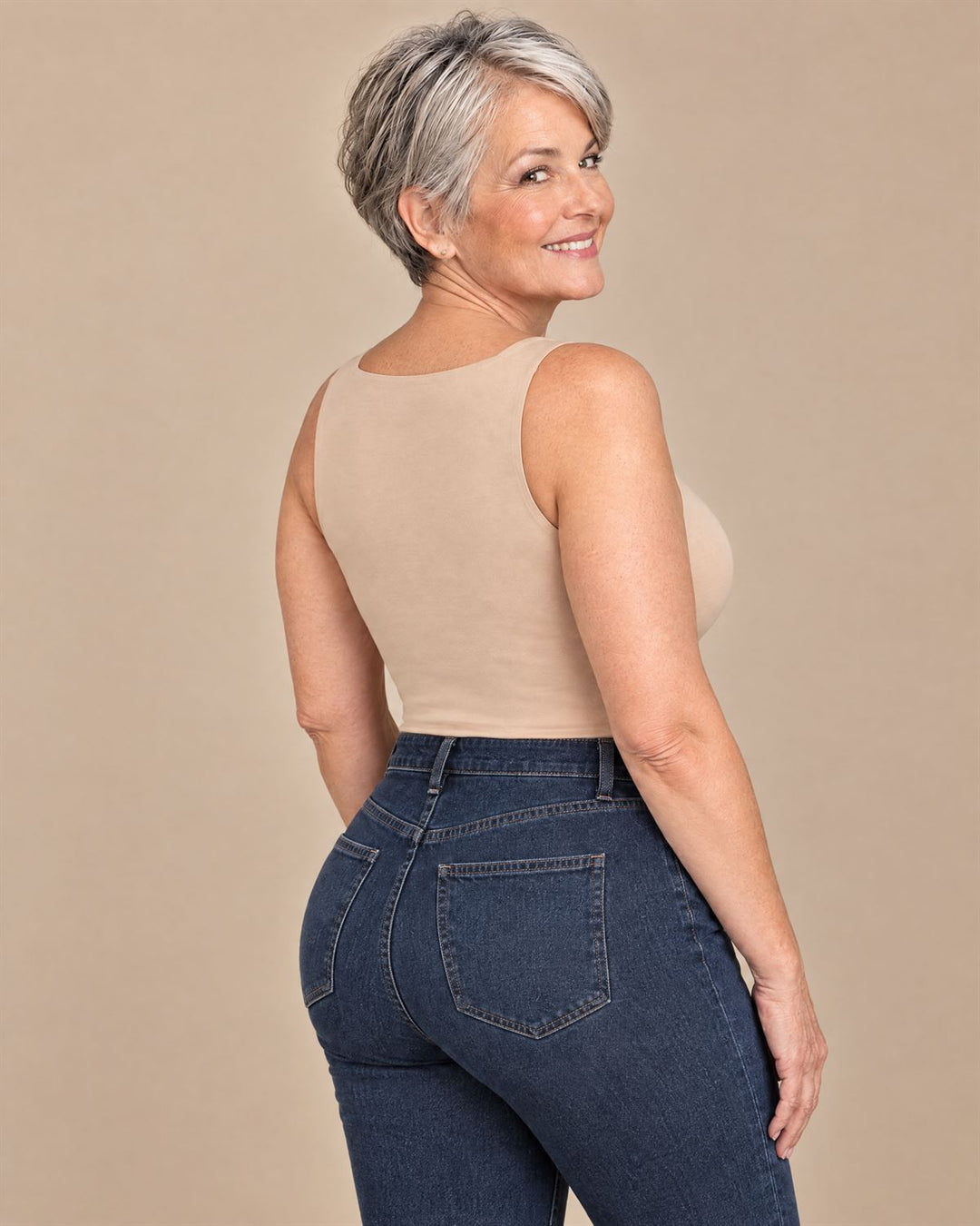 Curvy woman in her sixties with short silver hair in the nude tank, looking over her shoulder: a smooth, high back and a lifted bust