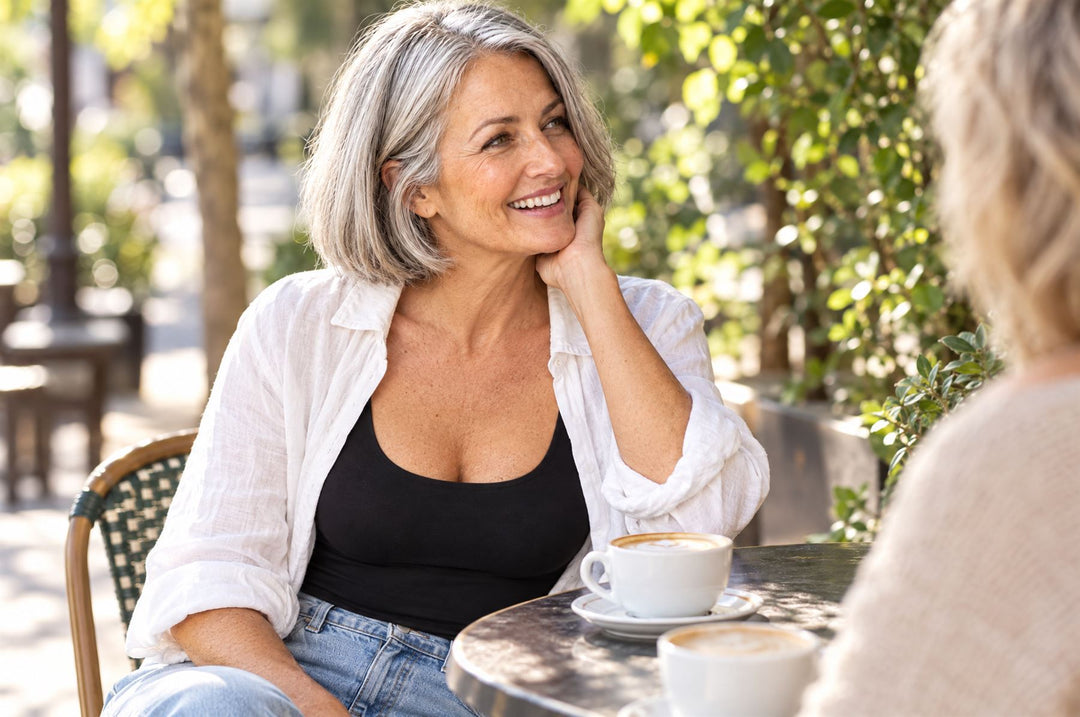 Woman laughing with a friend at a café, wearing a black tank under an open linen shirt