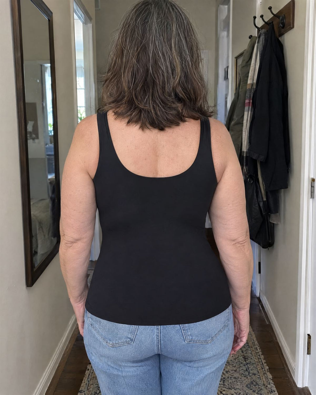 Woman in a black SmartFit tank, back view in a hallway: lies flat with no rolls