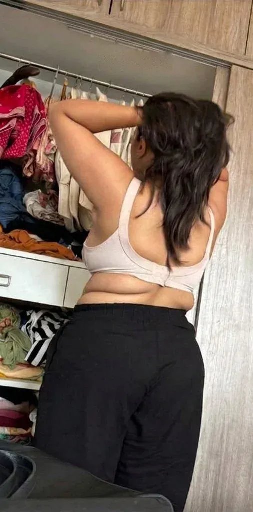 The same woman at her closet in a bra: the band digs in and pushes up a roll across her back