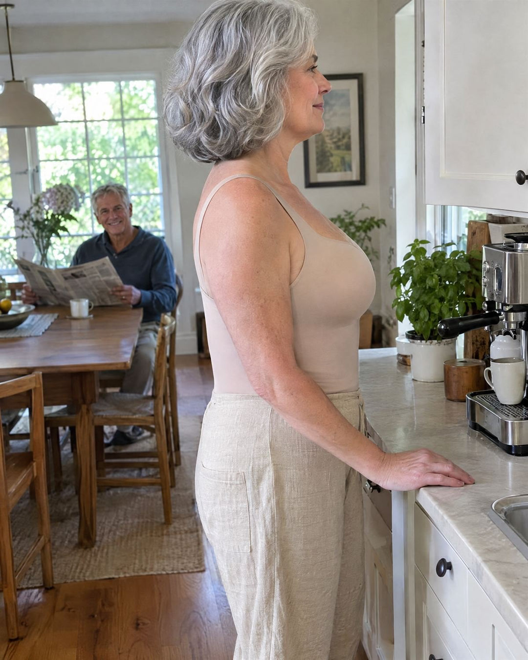 Woman in her sixties in a nude SmartFit tank in her kitchen, side view: lifted bust, upright posture