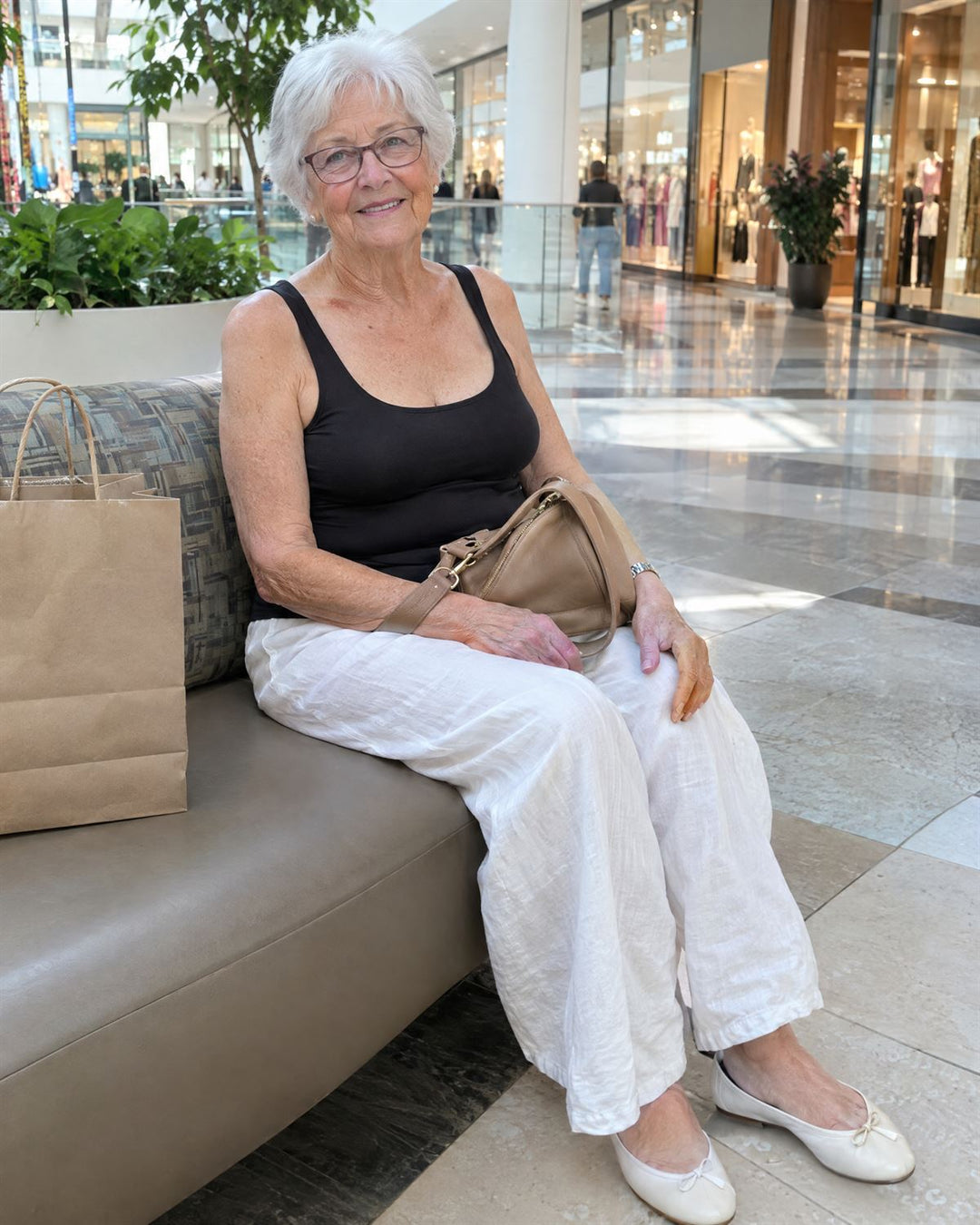 Woman in her eighties resting on a mall bench in a black tank and white linen trousers